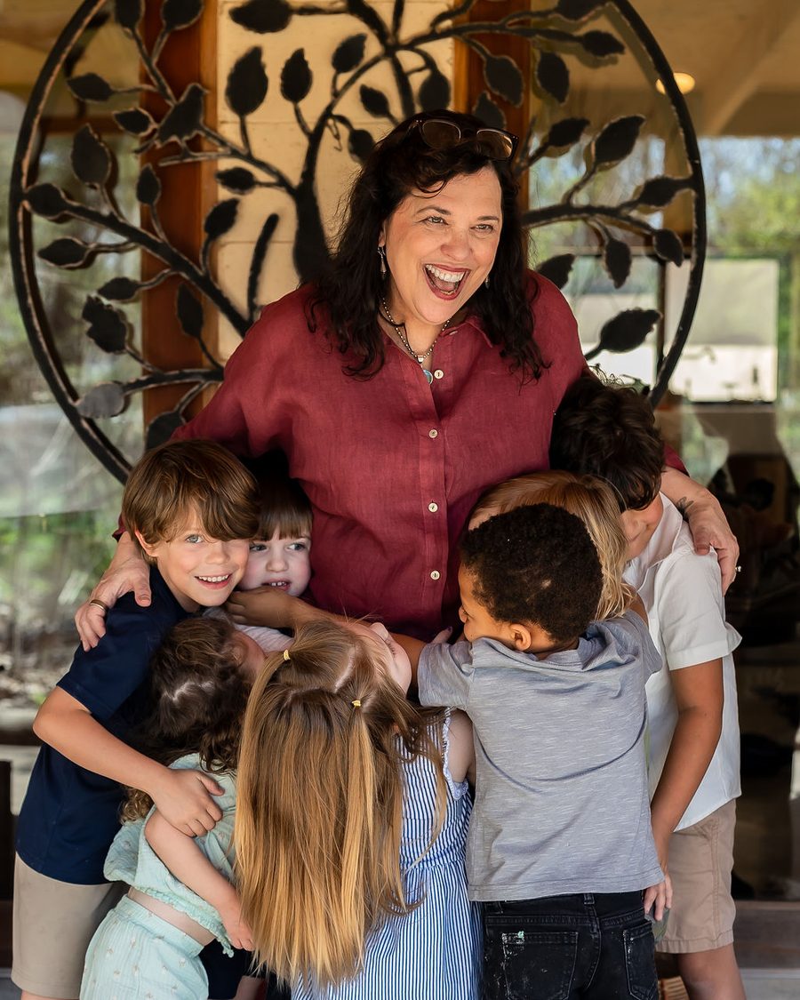Sally Haughey laughing as a group of children hug her